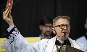 Ksiądz Michał Woźnicki w białej albie z koronkowymi mankietami podnosi obrazek, przemawiając do wiernych.