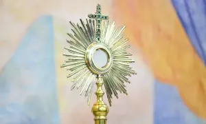 Monstrancja z hostią, symbol cudu w Lanciano, lśni na tle barwnych draperii.
