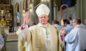 Biskup łódzki w białej mitrze i złotej szacie błogosławi wiernych, trzymając pastorał.