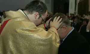 Kapłan w złotej szacie błogosławi mężczyznę. To ważny moment prymicji, pełen duchowej mocy.