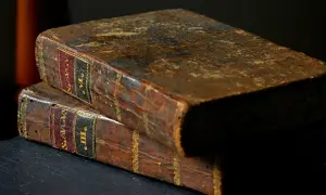 Dwa stare, skórzane tomy, jeden na drugim. Na grzbietach widoczne złote zdobienia i etykiety z łacińskimi napisami, sugerujące treść jak psalm 98.