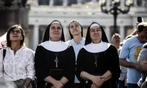 Dwie zakonnice w czarnych habitach z białymi kołnierzami patrzą w górę. Ich habit to symbol ich powołania.