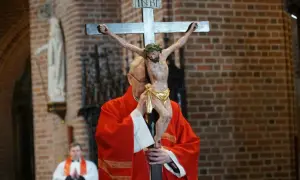Ksiądz w czerwonej szacie adoruje krzyż z figurą Chrystusa. Trwa liturgia Wielkiego Piątku, która jest wyrazem głębokiej refleksji.