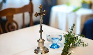 Krzyż, kropielnica z wodą i gałązka symbolizują błogosławieństwo.