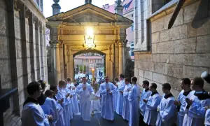 Uroczysta msza rezurekcyjna. Klerycy w białych szatach wychodzą z kościoła, niosąc paschał i kadzidło.