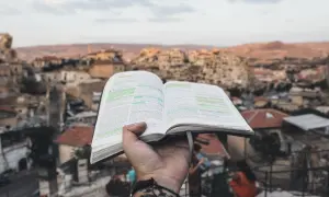 Otwarta księga z zaznaczonymi fragmentami, trzymana na tle starożytnego miasta. Może to być historia Izraelitów.