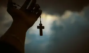 Dłoń trzyma paciorki różańca z krzyżem. Czy to symbol wiary, czy wątpliwości agnostyka, a może wyraz buntu ateisty?