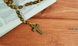 Różaniec na drewnianym stole obok Biblii, przypominający o 5 przykazaniach kościelnych.