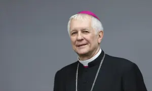 Uśmiechnięty biskup katowicki w stroju duchownym, z różowym zucchetto na głowie i srebrnym łańcuchem.