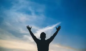 Sylwetka człowieka z rękami w górze na tle błękitnego nieba z chmurami. Jak w psalm 113, uwielbienie.