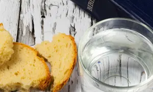 Chleb i woda na drewnianym stole, obok Biblii. Symbolika Wielkiego Piątku i postu.