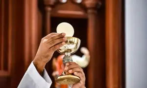 Kapłan w białej albie podnosi kielich z hostią, rozpoczynając liturgia eucharystyczna.