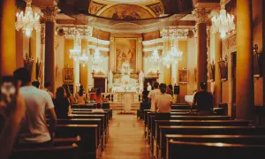 Wnętrze kościoła podczas mszy. Ludzie siedzą w ławkach, a przed ołtarzem trwa eucharystia.