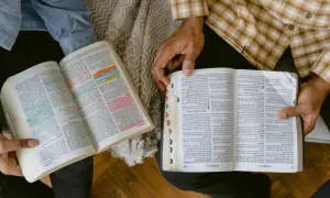Dwie osoby studiują Biblię, analizując podział ksiąg biblijnych. Widać fragmenty z kolorowymi zakreśleniami.