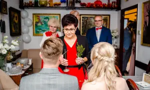 Krótkie błogosławieństwo pary młodej przez starszą panią z gałązką. W tle goście i dekoracje.