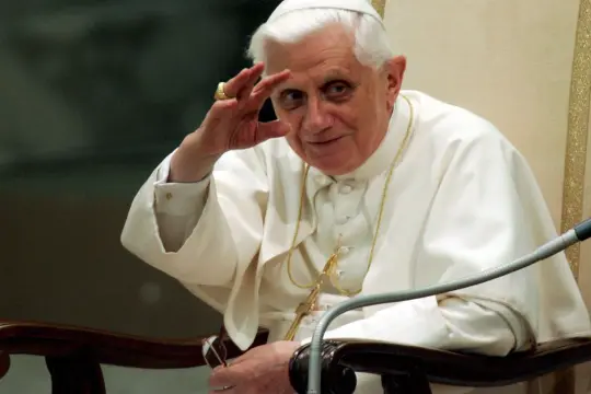 Papież Benedykt XVI, w białej sutannie, pozdrawia, jakby zapowiadając rewolucję seksualną.