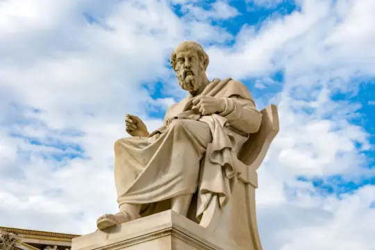 Kamienna rzeźba siedzącego mędrca, uosobienie neoplatonizmu, na tle błękitnego nieba z chmurami.