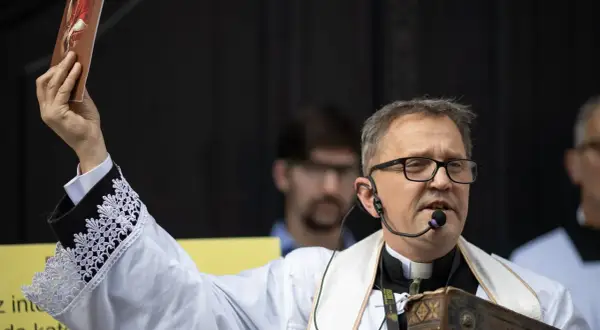 Ksiądz Michał Woźnicki w białej albie z koronkowymi mankietami podnosi obrazek, przemawiając do wiernych.