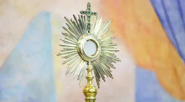 Monstrancja z hostią, symbol cudu w Lanciano, lśni na tle barwnych draperii.