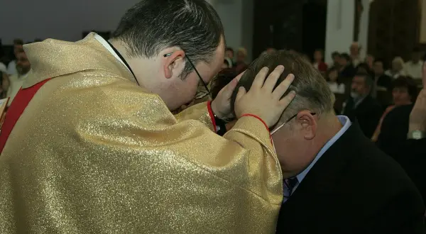 Kapłan w złotej szacie błogosławi mężczyznę. To ważny moment prymicji, pełen duchowej mocy.