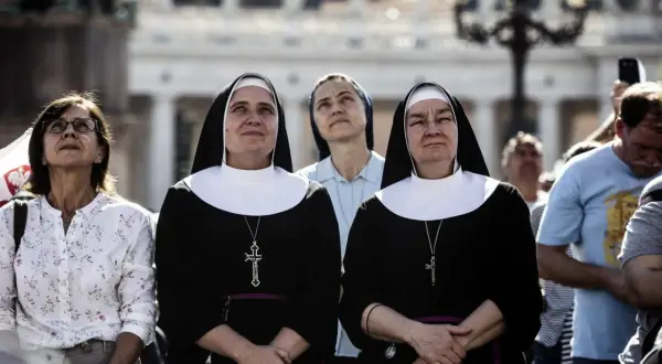 Dwie zakonnice w czarnych habitach z białymi kołnierzami patrzą w górę. Ich habit to symbol ich powołania.
