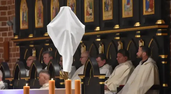 Biała tkanina unosi się nad klęczącymi duchownymi. Ceremonia bierzmowania trwa, a jej długość zależy od wielu czynników.