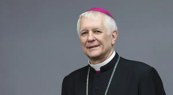 Uśmiechnięty biskup katowicki w stroju duchownym, z różowym zucchetto na głowie i srebrnym łańcuchem.