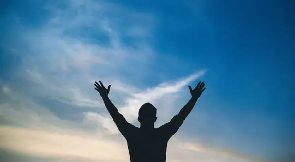 Sylwetka człowieka z rękami w górze na tle błękitnego nieba z chmurami. Jak w psalm 113, uwielbienie.