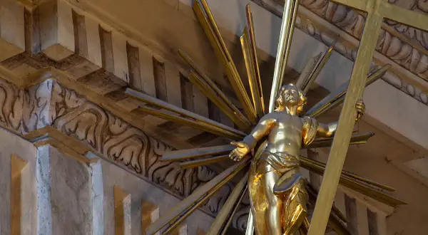 Złoty posąg Chrystusa z krzyżem, otoczony promieniami. Jego postawa mówi: "Jestem który jestem".