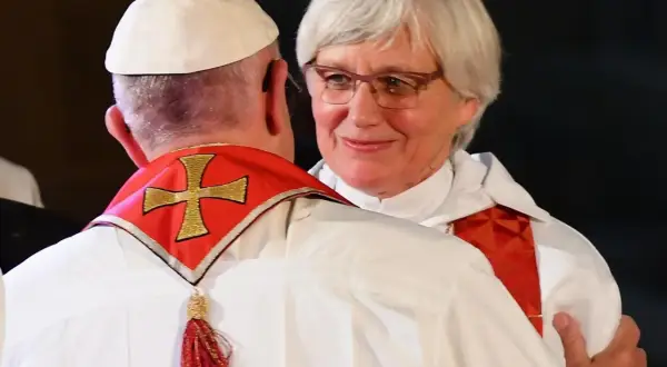 Kobieta ksiądz w okularach uśmiecha się, obejmując papieża.