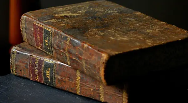 Dwie stare, skórzane księgi, jedna na drugiej. Na grzbietach widoczne napisy, sugerujące zawartość, być może mądrość Salomona z Biblii.