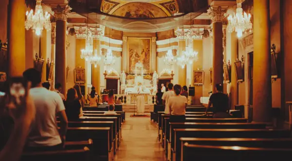 Wnętrze kościoła podczas mszy. Ludzie siedzą w ławkach, a przed ołtarzem trwa eucharystia.
