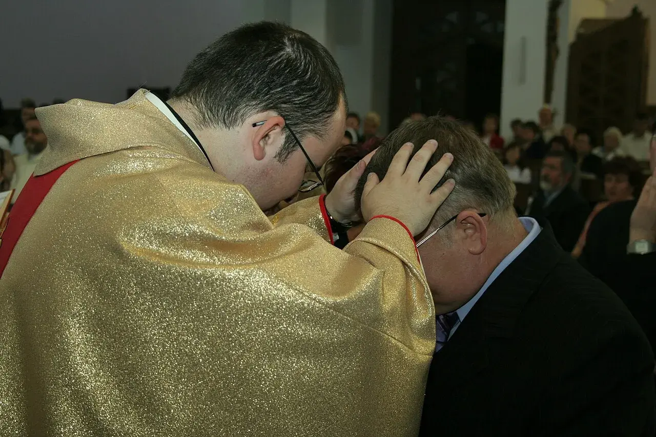 Kapłan w złotej szacie błogosławi mężczyznę. To ważny moment prymicji, pełen duchowej mocy.