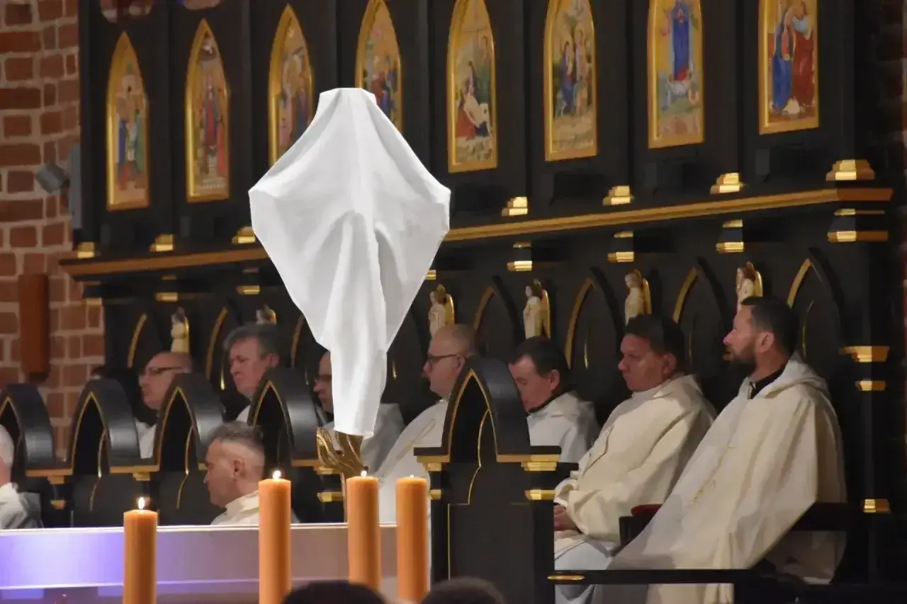 Biała tkanina unosi się nad klęczącymi duchownymi. Ceremonia bierzmowania trwa, a jej długość zależy od wielu czynników.