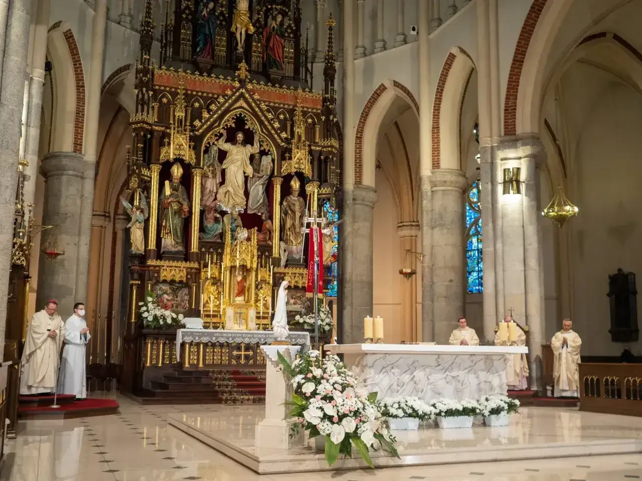 W kościele trwa msza. 1 maja święto kościelne, kapłani w szatach liturgicznych przy ołtarzu.