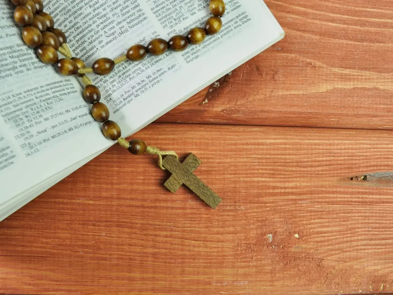 Różaniec na drewnianym stole obok Biblii, przypominający o 5 przykazaniach kościelnych.