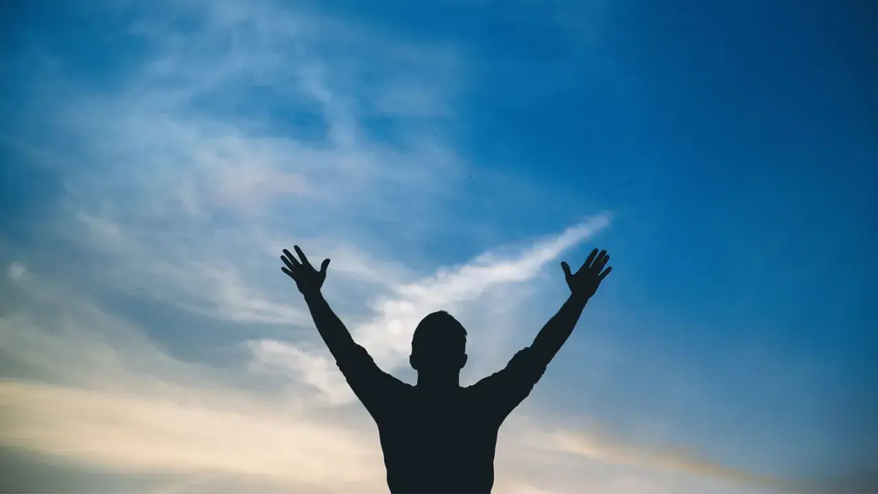 Sylwetka człowieka z rękami w górze na tle błękitnego nieba z chmurami. Jak w psalm 113, uwielbienie.