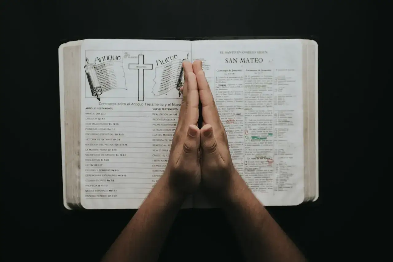 Dłonie złożone do modlitwy nad otwartą Biblią, z widocznym porównaniem Starego i Nowego Testamentu. W sercu tej chwili, jak w psalmie 9, szukamy pocieszenia.