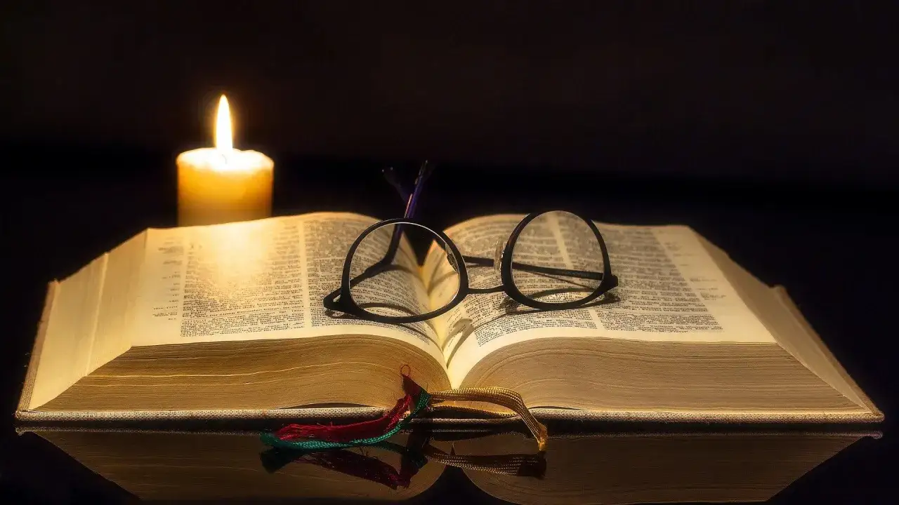 Świeca oświetla otwartą księgę z okularami, gdzie można odnaleźć najpiękniejsze psalmy.