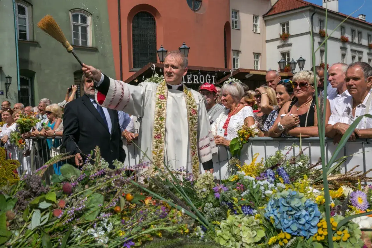 Uroczystość 15 sierpnia święto kościelne. Ksiądz święci bukiety z ziół i kwiatów, tłum obserwuje.