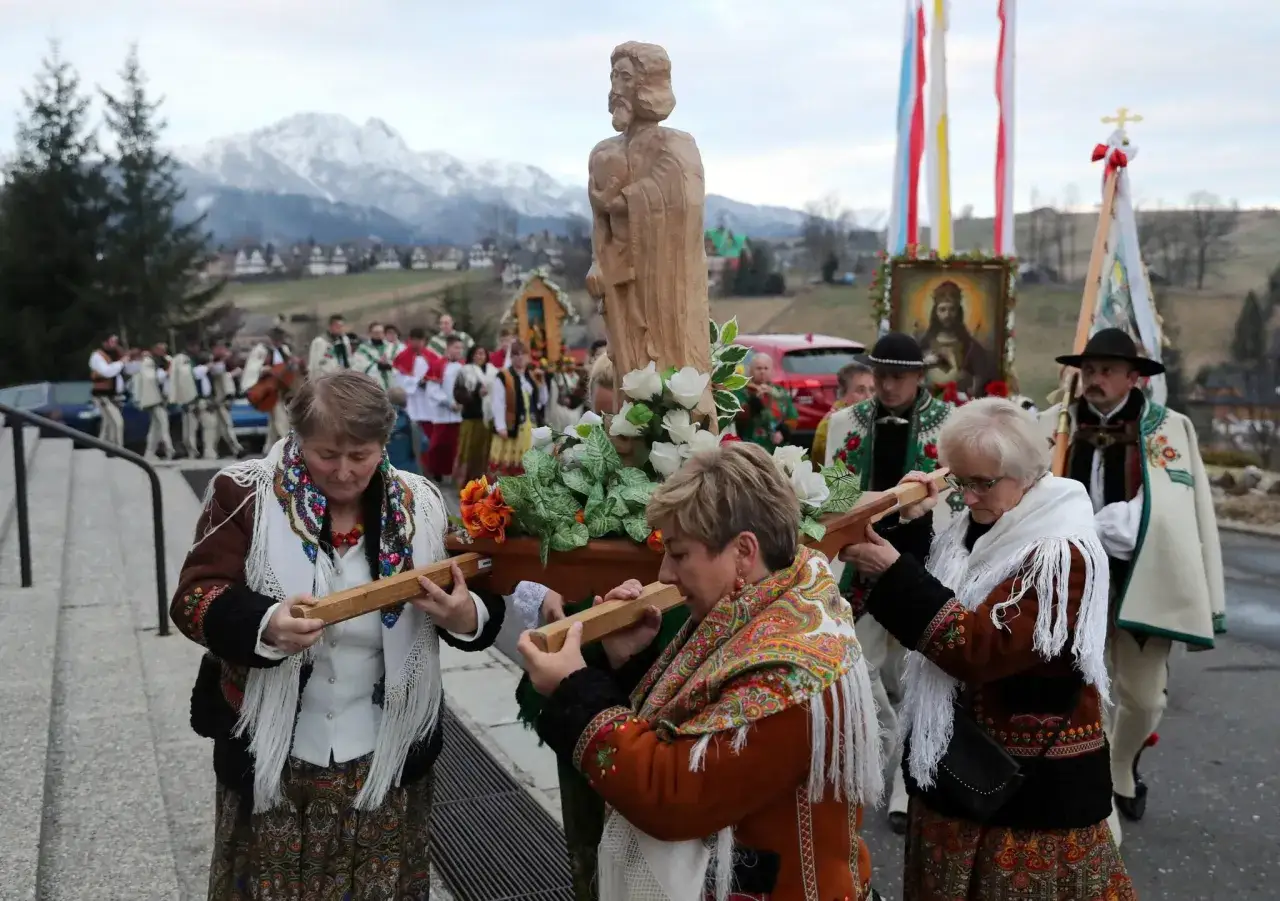 Uroczysta rezurekcja w góralskich strojach. Ludzie niosą drewnianą figurę Chrystusa, za nimi procesja z obrazem i flagami.