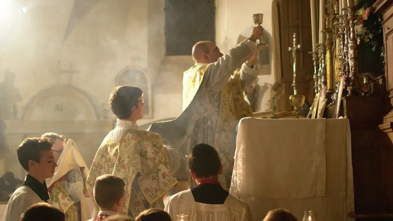 Lefebryści podczas mszy. Kapłan podnosi kielich, ministranci w ornacie z kwiatowym wzorem asystują.