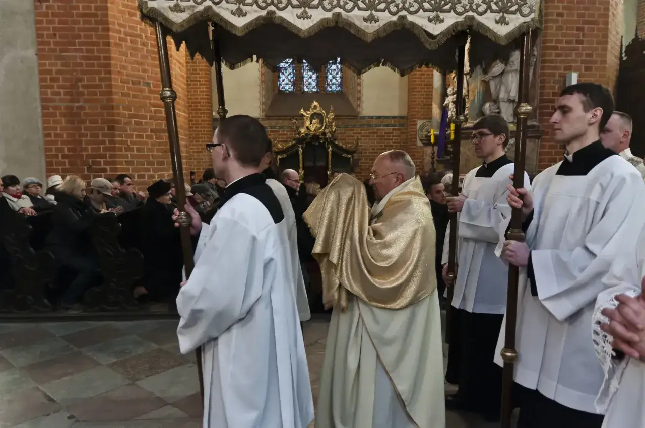 Uroczysta procesja w kościele. Klerycy w białych szatach niosą chorągwie. Złota szata kapłana sugeruje ważność wydarzenia, być może związanego z tym, ile trwaja rezurekcje.