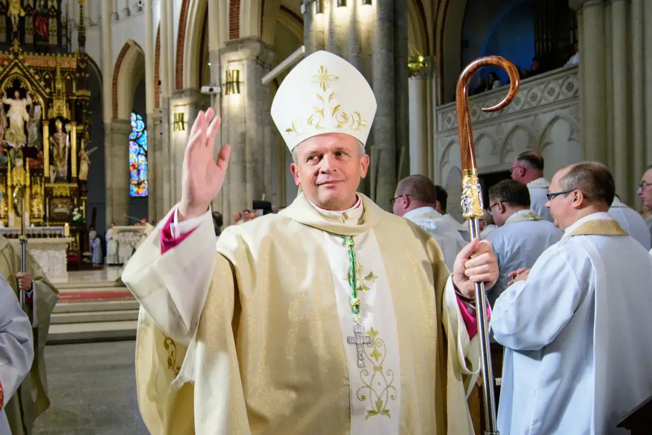 Biskup łódzki w białej mitrze i złotej szacie błogosławi wiernych, trzymając pastorał.