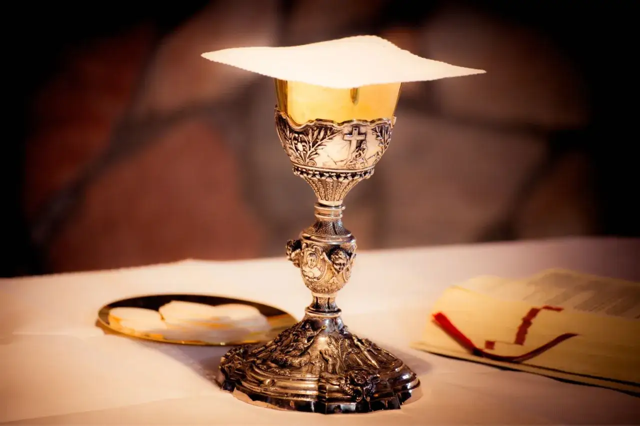 Oto kielich z hostią, symbol Eucharystii. Obok leży książka, być może modlitewnik.