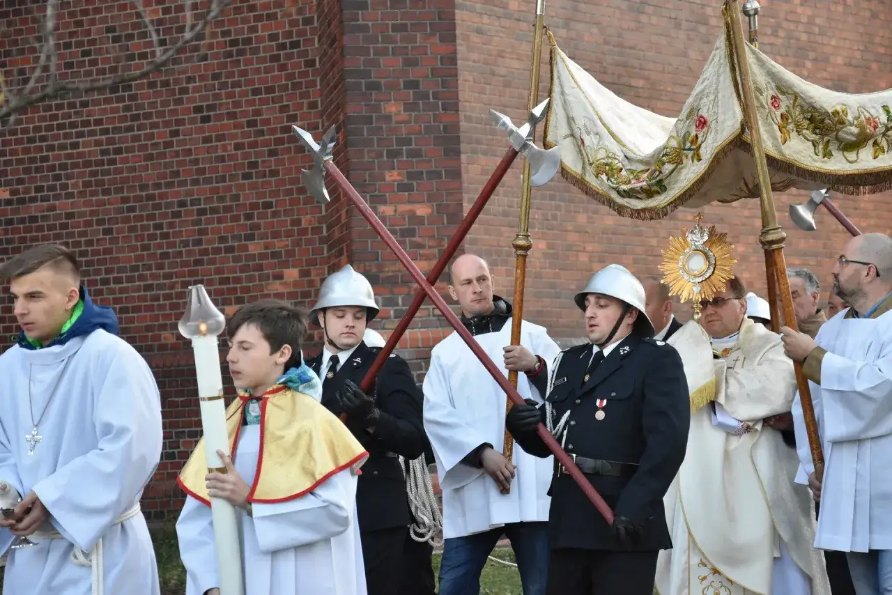 Uroczysta msza rezurekcyjna z procesją. Mężczyźni w strojach liturgicznych niosą monstrancję i chorągwie.