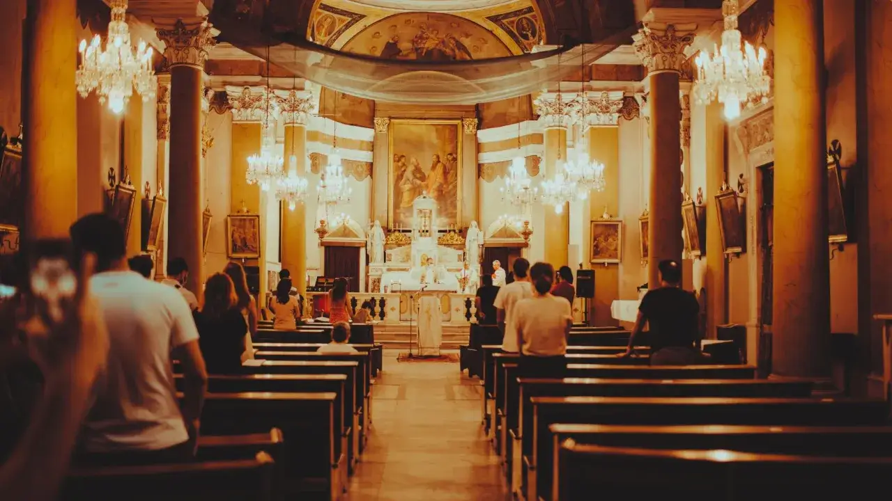 Wnętrze kościoła podczas mszy. Ludzie siedzą w ławkach, a przed ołtarzem trwa eucharystia.