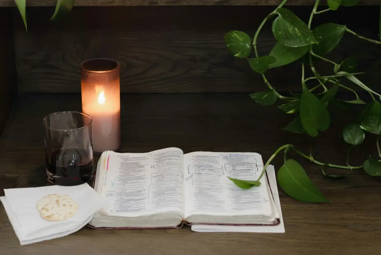 Otwarta Biblia, kielich z winem, opłatek i płonąca świeca. Wersety biblijne na stronach zapraszają do refleksji.