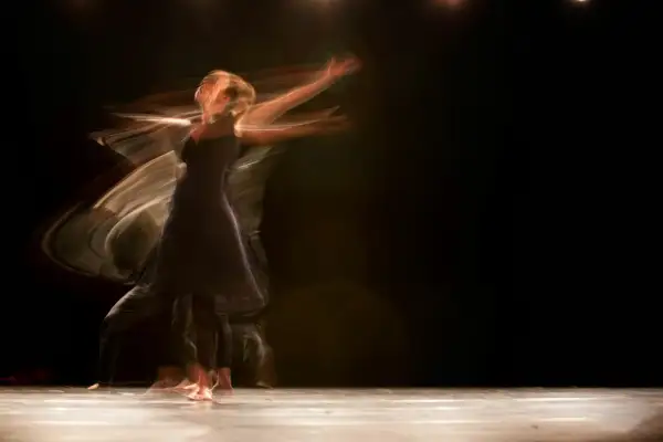 Tancerka w ciemnej sukience wiruje na scenie, jej ruchy rozmyte w świetle. Czy dusza tęskni za wolnością?