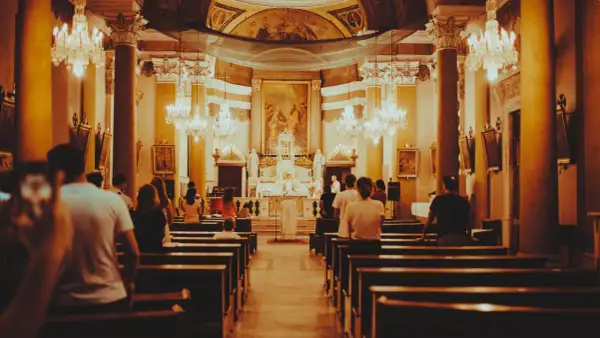 Wnętrze kościoła podczas mszy. Ludzie siedzą w ławkach, a przed ołtarzem trwa eucharystia.